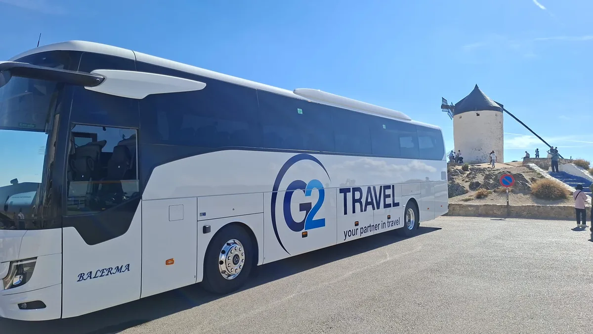Autocar blanco con rotulación G2 Travel y nombre Balerma junto a un molino de viento.