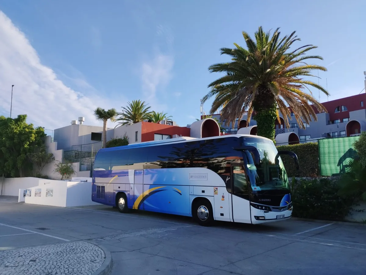 Autocar Balerma con decoración azul y amarilla, estacionado junto a un hotel con palmeras.